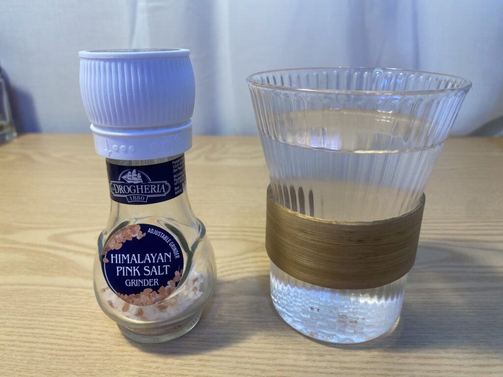 A glass mug of warm salt water on a wooden table, representing the Korean actress morning beauty routine for glowing skin and reducing bloating.