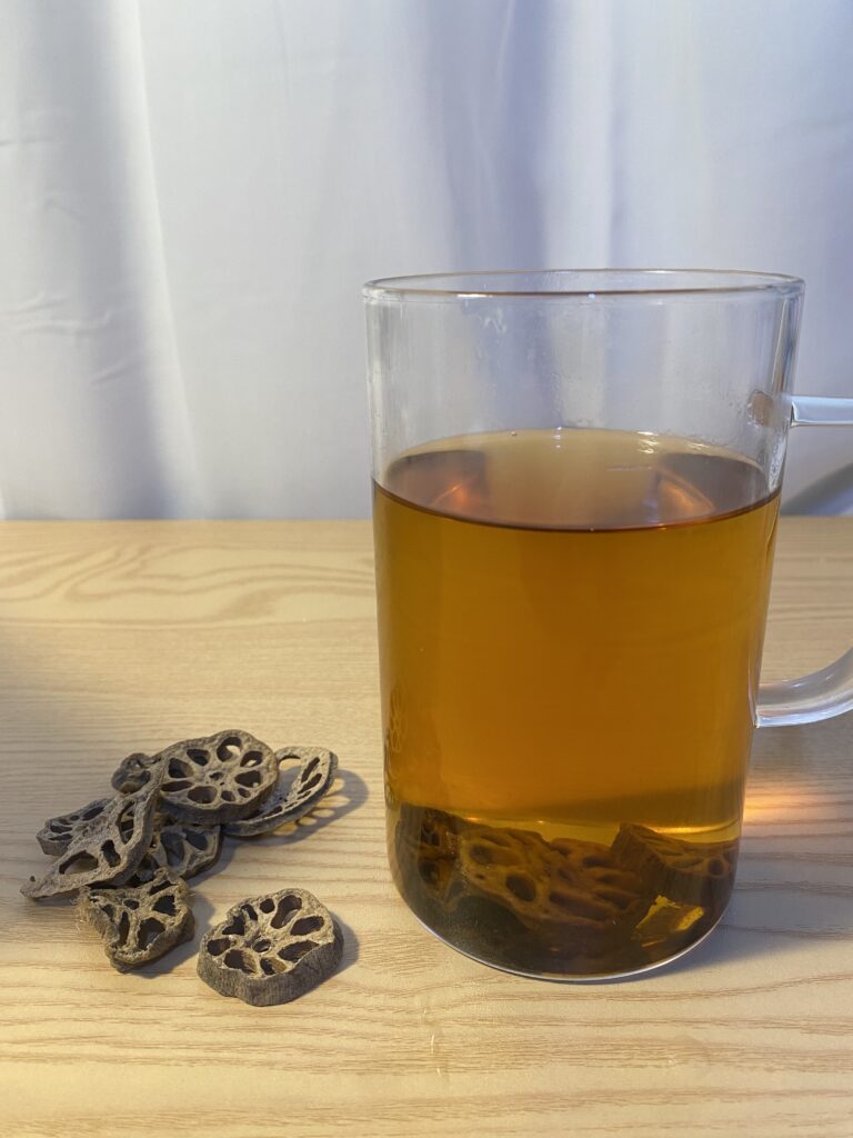 A clear glass cup showing 3 slices of roasted lotus root steeping in hot water.