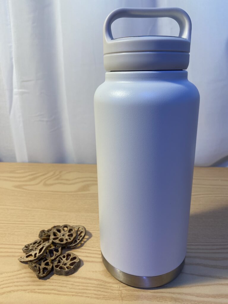 A thermal tumbler on a professional desk next to dried lotus root slices.