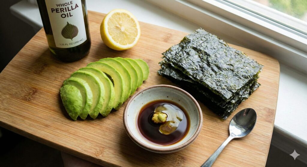 Fresh sliced avocado, crispy roasted seaweed sheets, a small bowl of wasabi soy sauce, and perilla oil arranged on a clean wooden board.