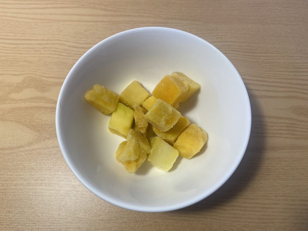 A close-up shot of slightly thawed frozen mango chunks in a glass bowl, showing a creamy, sorbet-like texture that serves as a perfect natural alternative to ice cream.