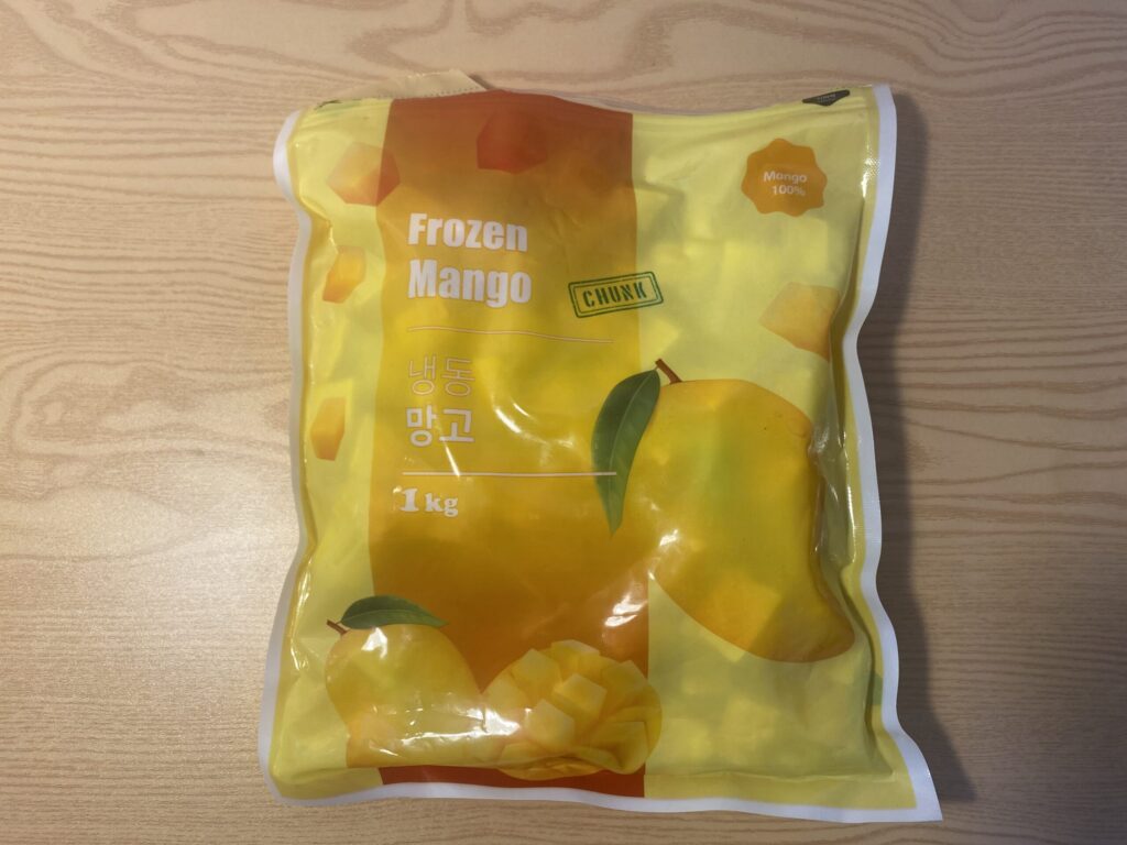 A close-up shot of slightly thawed frozen mango chunks in a glass bowl, showing a creamy, sorbet-like texture that serves as a perfect natural alternative to ice cream.