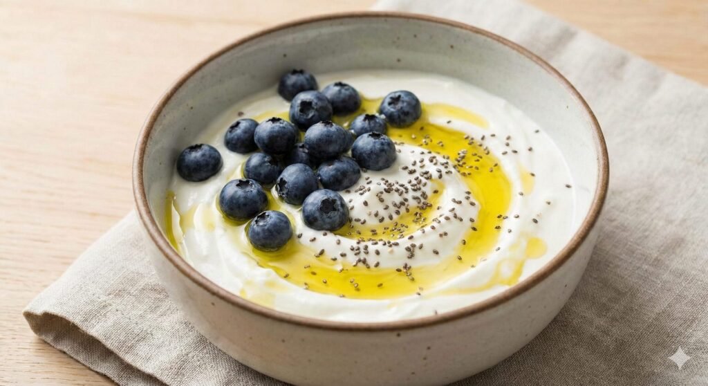 A bowl of Greek yogurt topped with fresh blueberries, a drizzle of olive oil, and chia seeds, representing a biohacking synbiotic meal for gut health.
