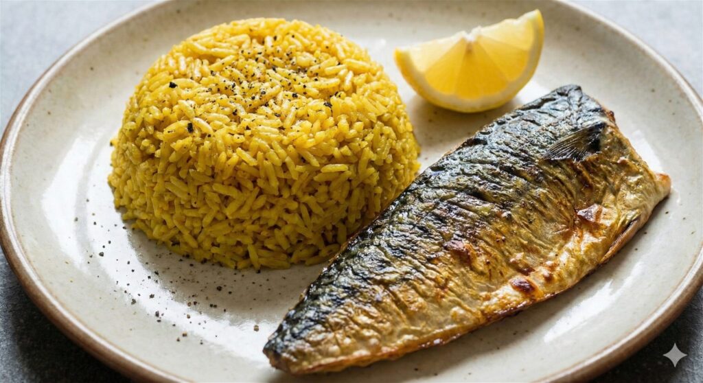  A plate featuring vibrant yellow turmeric rice infused with black pepper and coconut oil, served next to a perfectly grilled, crispy-skinned mackerel fillet with a lemon slice.