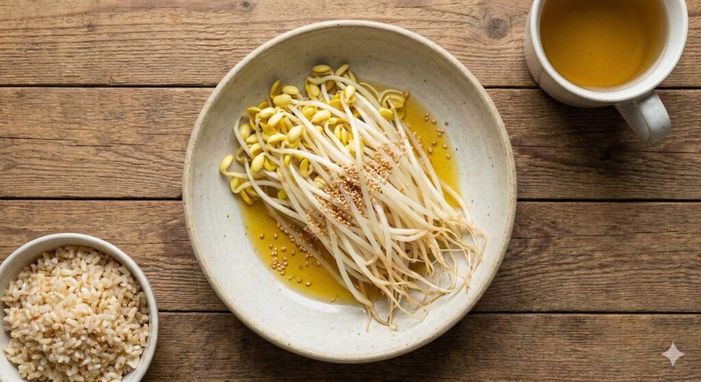 A top-down view of a minimalist biohacking meal on a rustic wooden table. A ceramic bowl holds lightly steamed whole soybean sprouts (roots intact) drizzled with golden perilla oil and sesame seeds, served alongside brown rice and herbal tea.