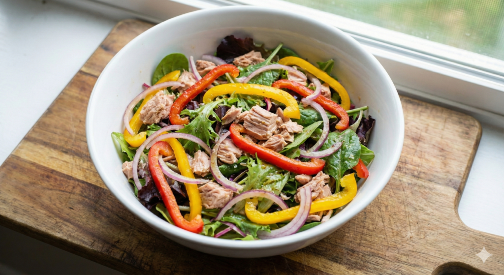 참치 조각과 다채로운 파프리카 슬라이스, 채소가 드레싱에 가볍게 버무려진 생동감 넘치는 파프리카 참치 샐러드 볼. 빠르고 조리가 필요 없는 항염증 바이오해킹 식단을 나타냄.