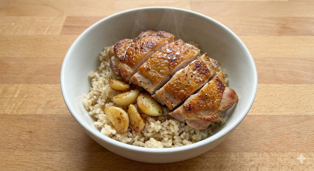 A masterfully prepared biohacking bowl featuring a perfectly seared, juicy chicken thigh and deeply roasted, golden-brown whole garlic cloves served over a bed of cooled brown rice, representing sustained mitochondrial energy.